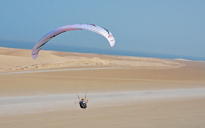 رجل يمارس القفز المظلي في قطر وفي الاسفل توجد رمال