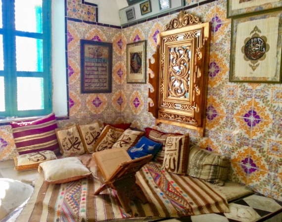 غرفة ذات جدار ملون ومزخرف واماكن للجلوس في متحف دار العنابي في تونس