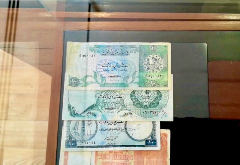 عروض لعملات قطرية قديمة موضوعة تحت زجاج، تتضمن ورقة مالية من فئة العشرة ريالات وأخرى بفئات مختلفة.